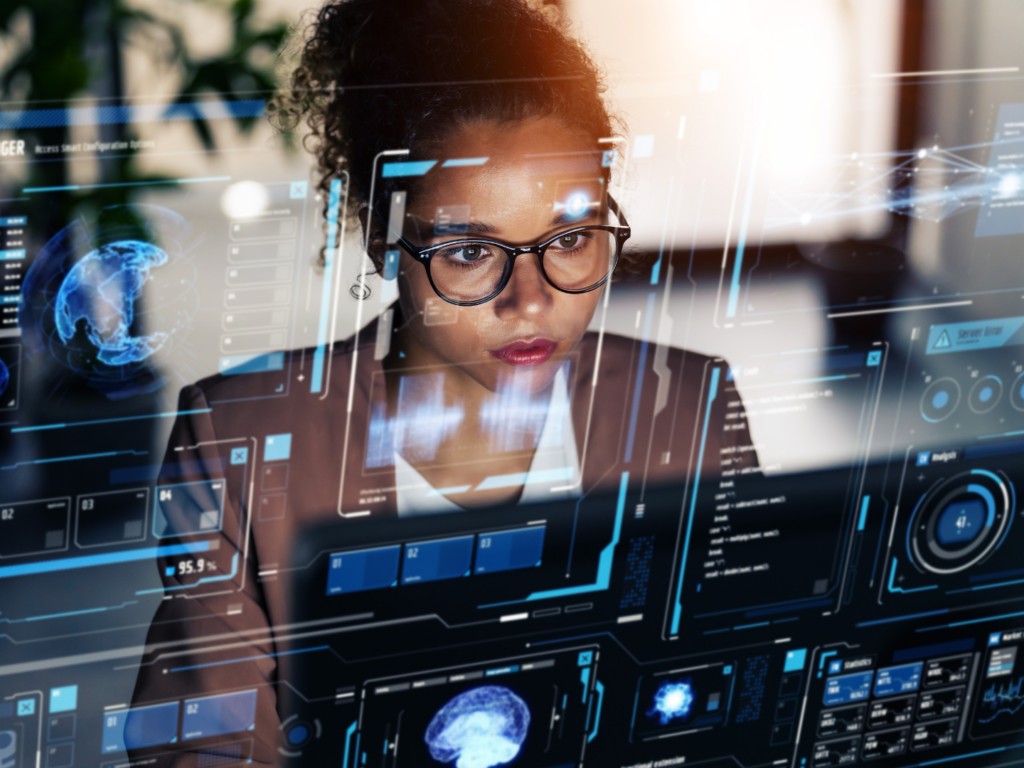 a dark skinned woman with glasses looks at a computer screen with multiple windows outlining cyber security surveillance that partners with her cyber security liability insurance policy