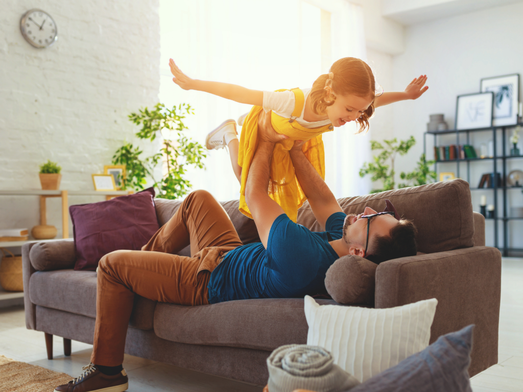 a father and daughter playing on the couch in the living room of their home that is protected after reading why to review your homeowners insurance coverage